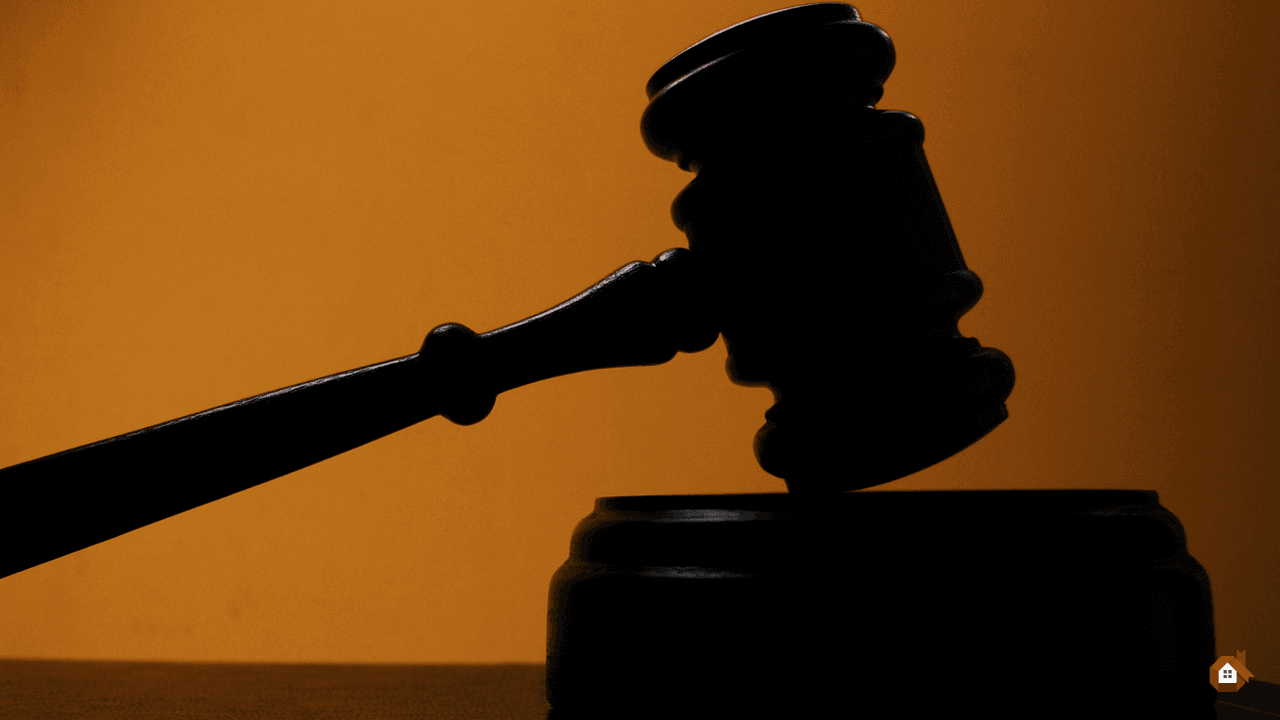 Silhouette noire d'un marteau de juge en bois sur son socle devant un arrière-plan orange uni
