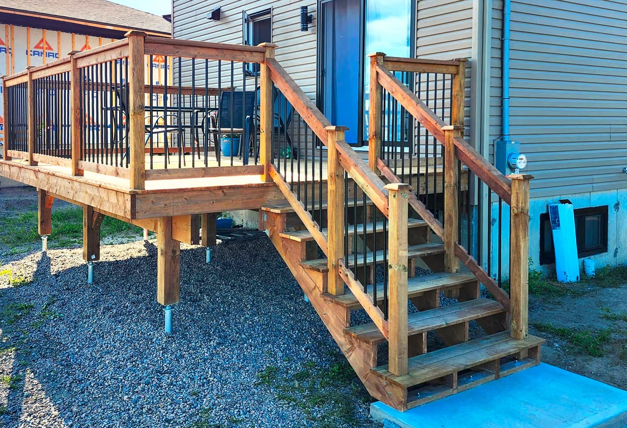 Patio en bois avec escalier, rampes noires et revêtement extérieur de maison résidentielle
