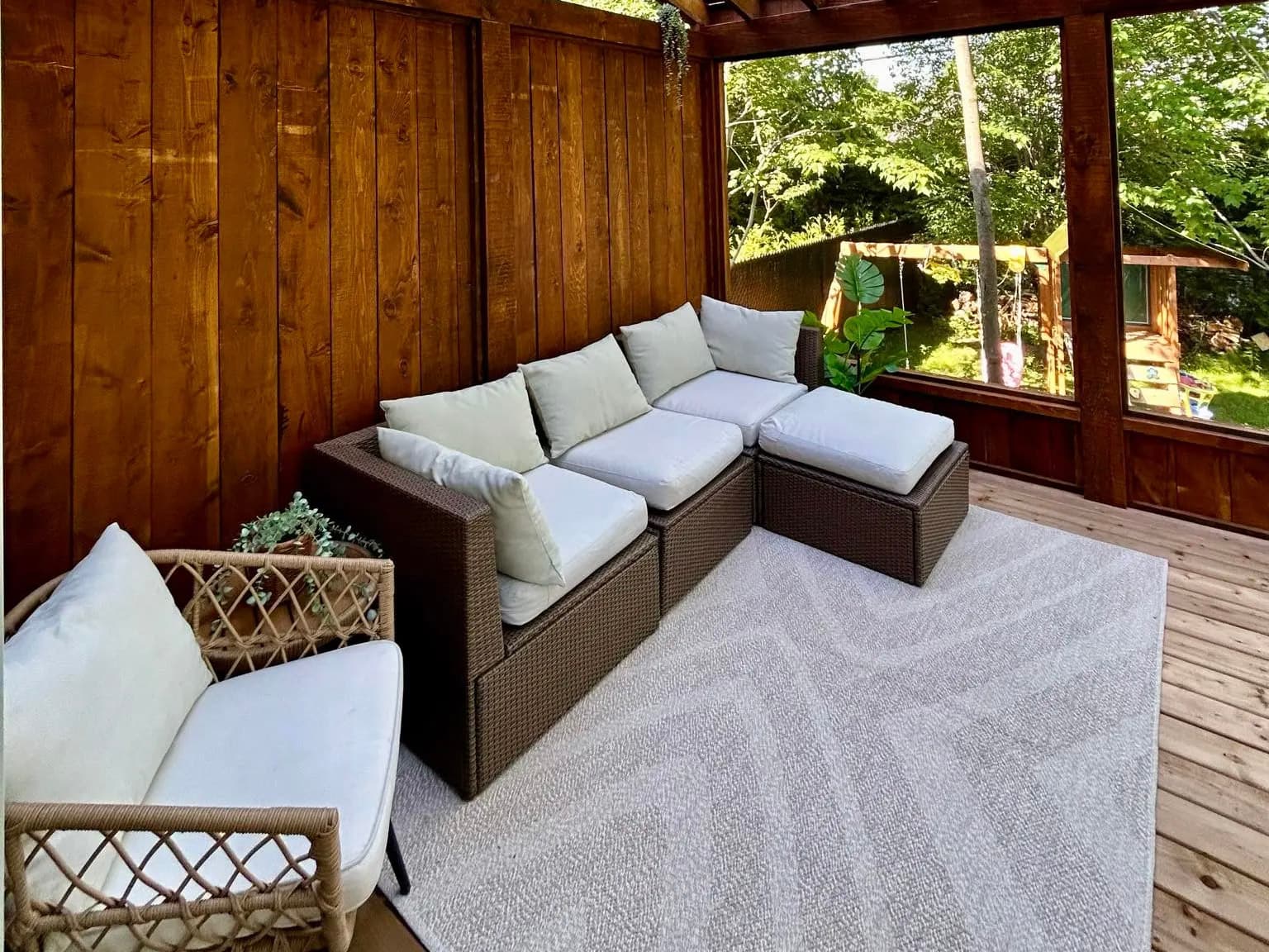 Pergola en bois avec terrasse couverte, mobilier extérieur et coussins blancs dans un cadre naturel.