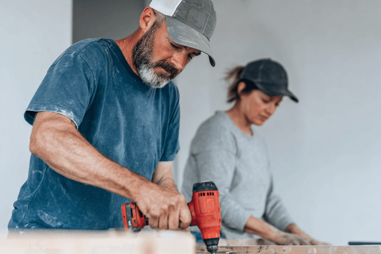 Travailleurs en rénovation intérieure utilisant une perceuse électrique sur une structure en bois dans une pièce en chantier