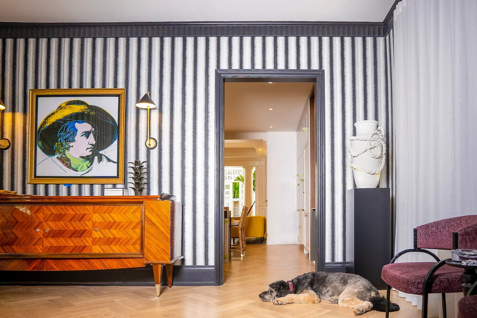 Intérieur sophistiqué avec papier peint à rayures, mobilier de designer en bois et plancher de parquet à chevrons.