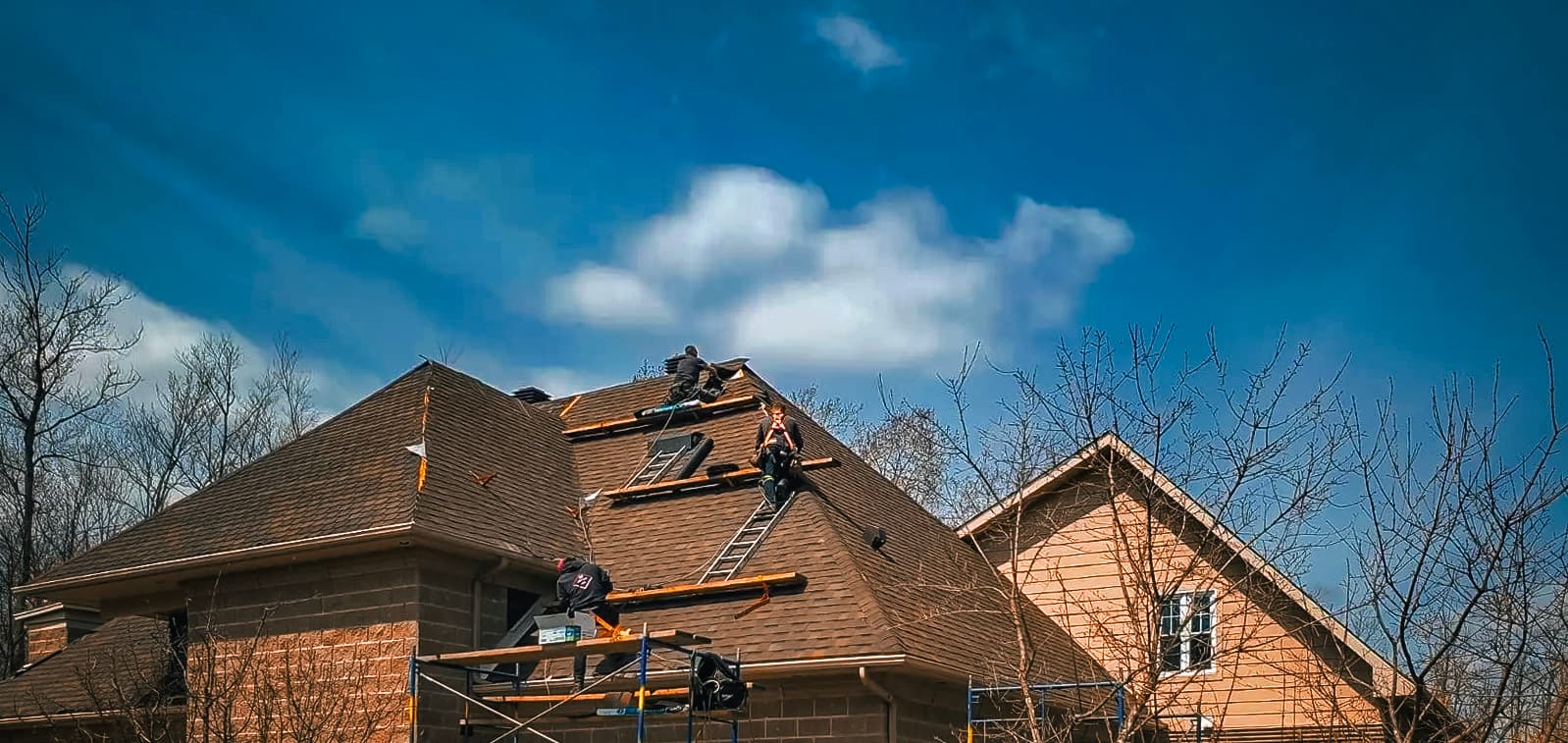 Des couvreurs travaillent sur un toit en pente sous un ciel bleu, installant des bardeaux et rénovant une maison.