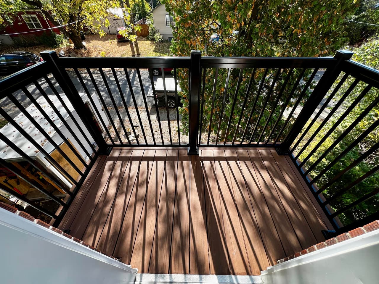 Balcon extérieur avec plancher en bois composite brun et garde-corps noir donnant sur une rue bordée d’arbres.