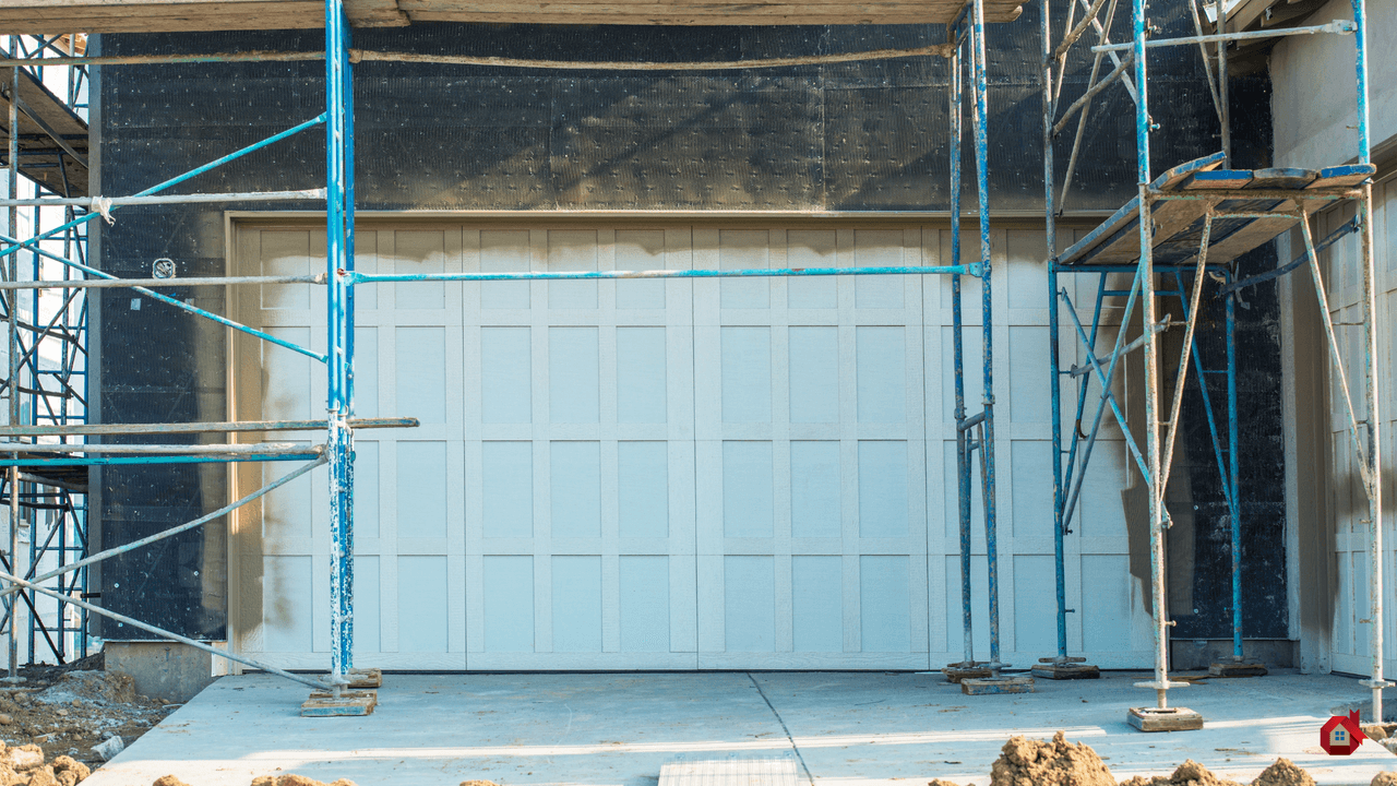 Porte de garage blanche à panneaux nouvellement installée sur une maison en construction, entourée d'échafaudages métalliques