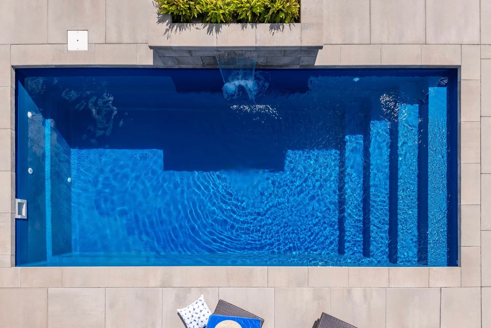 Vue aérienne d'une piscine rectangulaire avec cascade intégrée, entourée de dalles modernes et de végétation décorative.