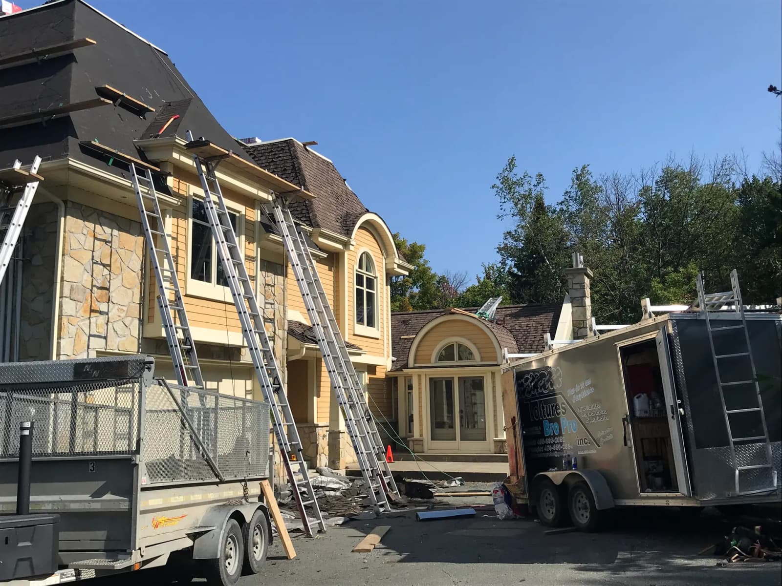 Maison moderne en bois avec un toit en métal, entourée de grands arbres et baignée de soleil dans un cadre naturel boisé