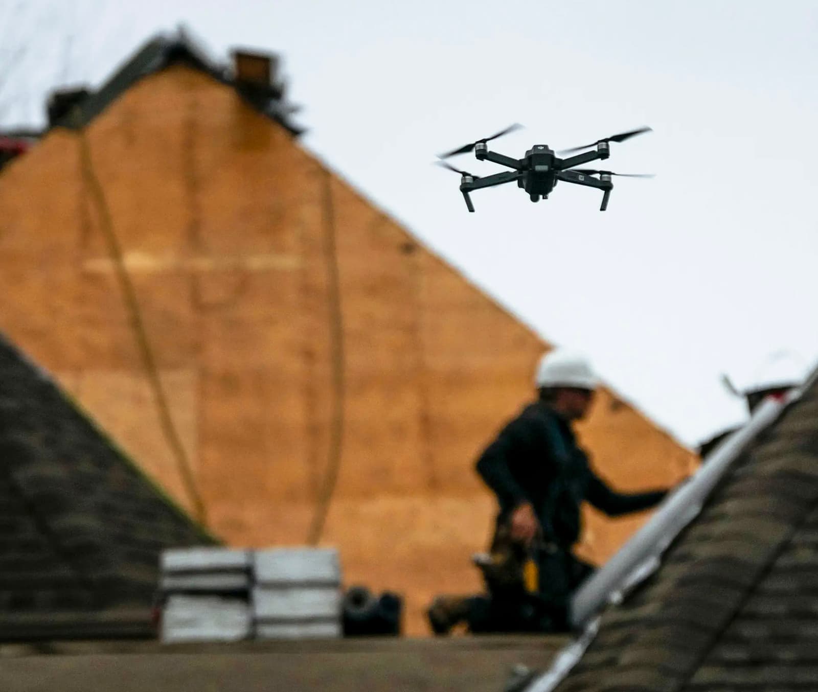 Drone en vol au-dessus d’un chantier de toiture où des travailleurs avec casques effectuent des rénovations.