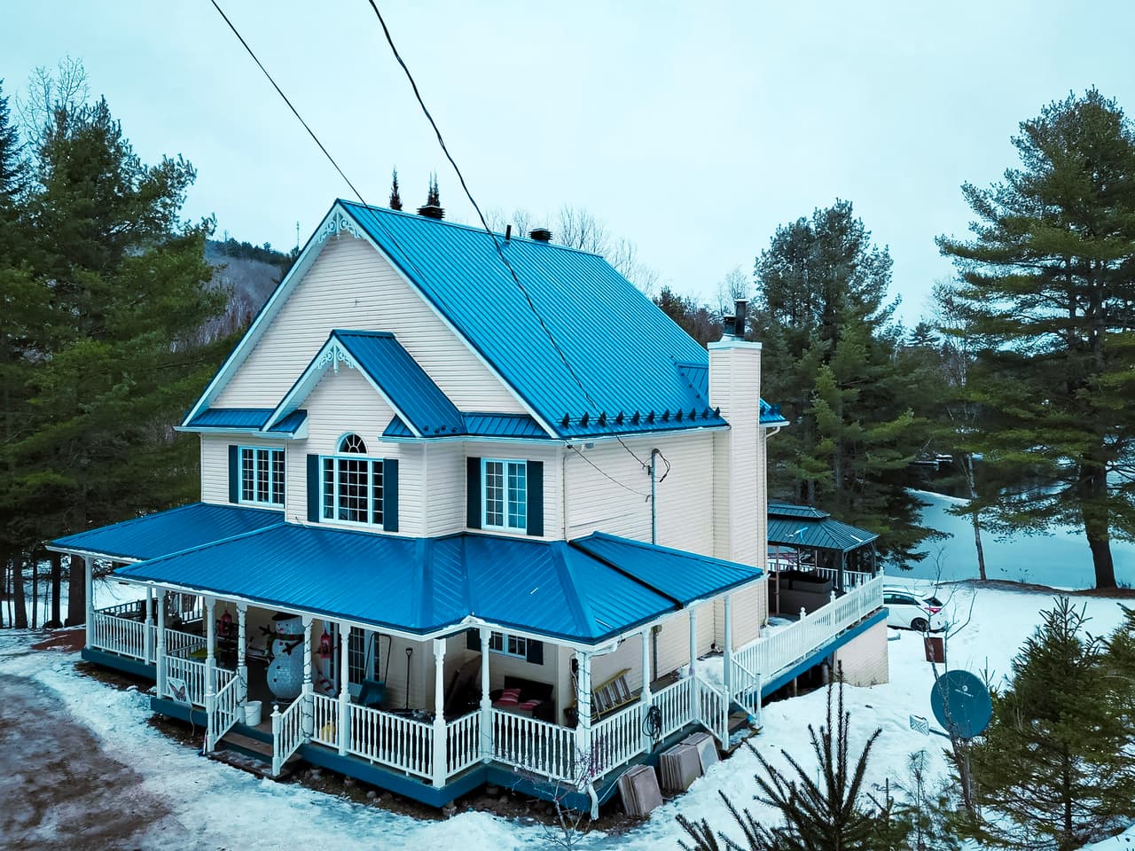 Maison de style victorien rénovée avec une toiture métallique bleue et une grande galerie couverte en hiver