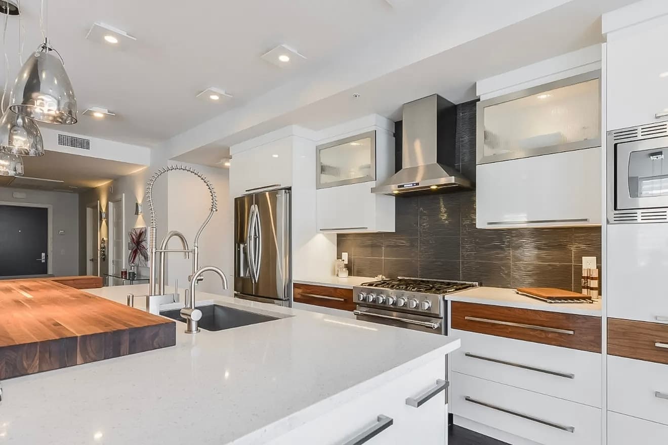 Cuisine moderne avec îlot central en quartz, électroménagers en acier inoxydable et luminaires suspendus pour un design épuré et contemporain.