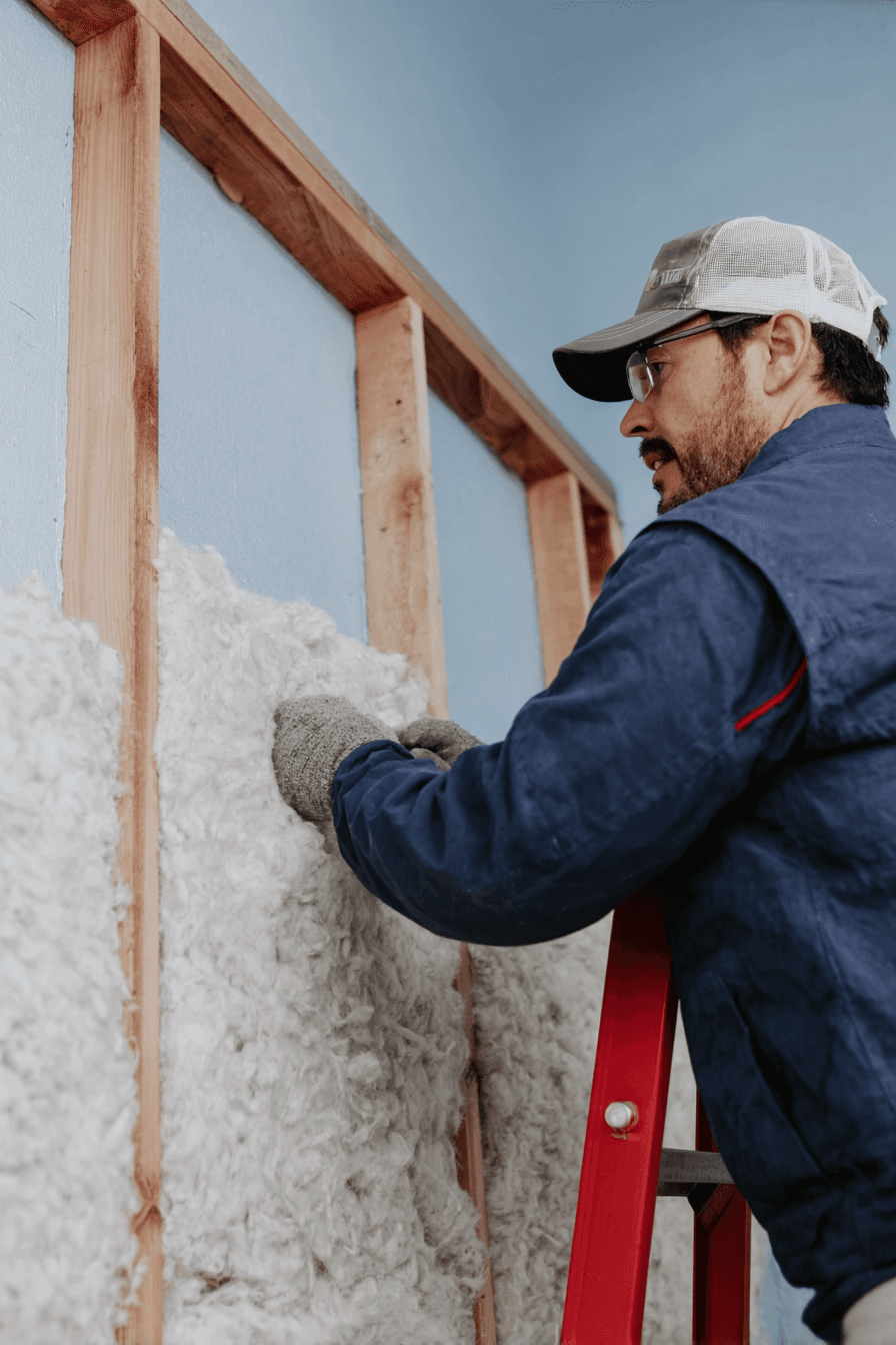 Travailleur installant de l’isolant en fibres dans une cloison intérieure à ossature de bois pour améliorer l’isolation thermique et acoustique d’une maison