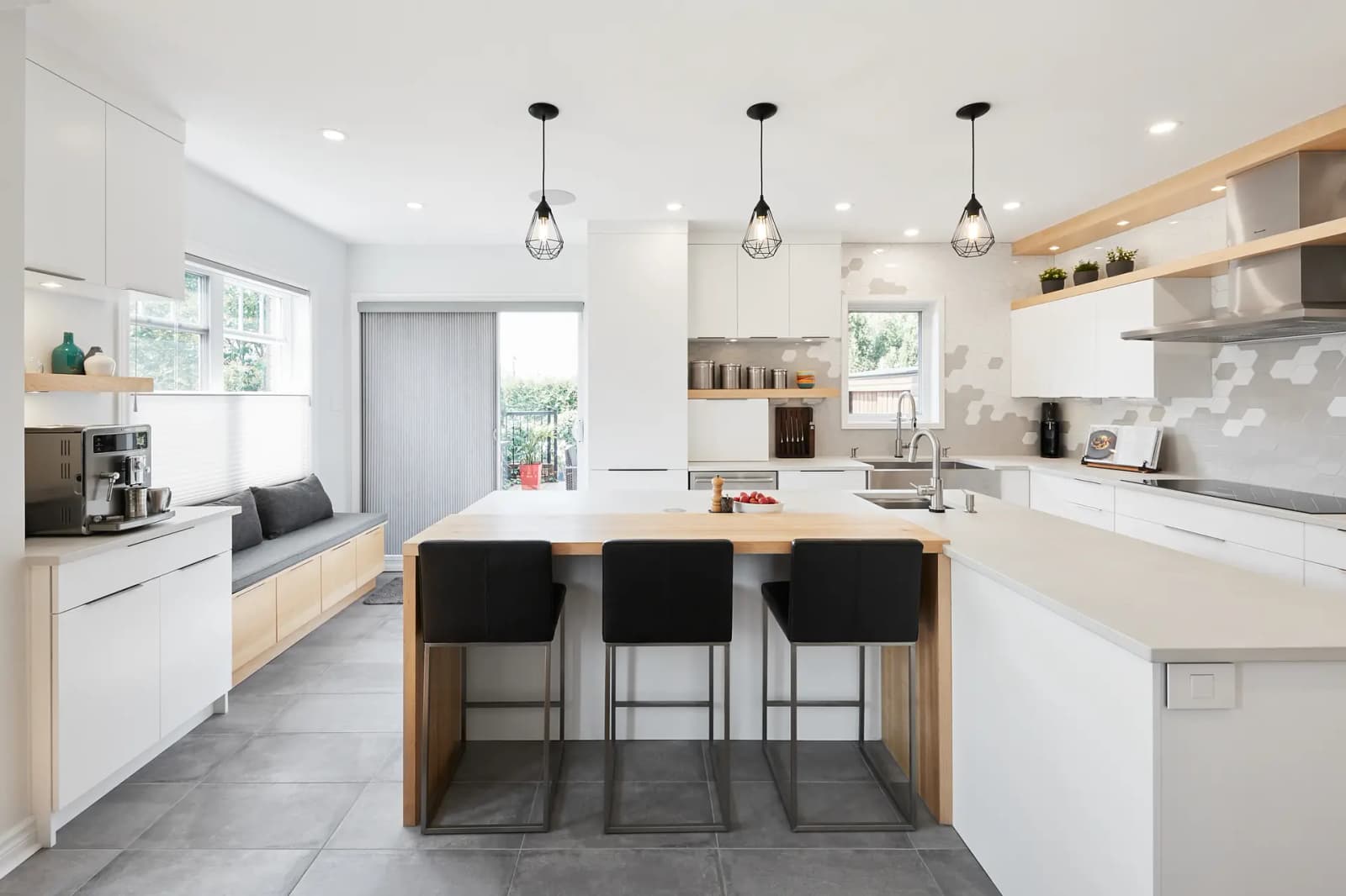 Cuisine de style scandinave à Montréal, mettant en valeur un îlot central spacieux avec des barstools noirs, des armoires blanches minimalistes et un dosseret en mosaïque géométrique. Le plancher en céramique gris ajoute une touche de chaleur à l'espace