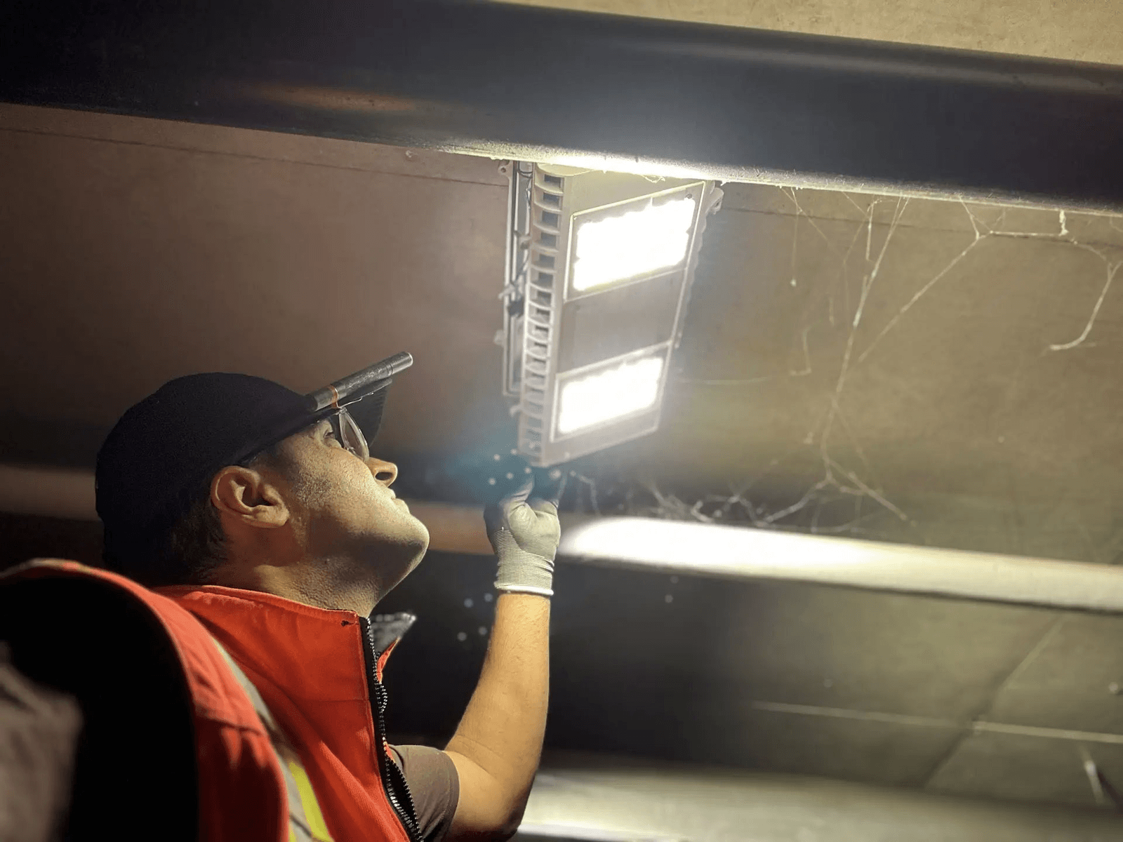 Technicien en éclairage inspectant ou ajustant un luminaire LED installé au plafond dans un espace intérieur sombre.
