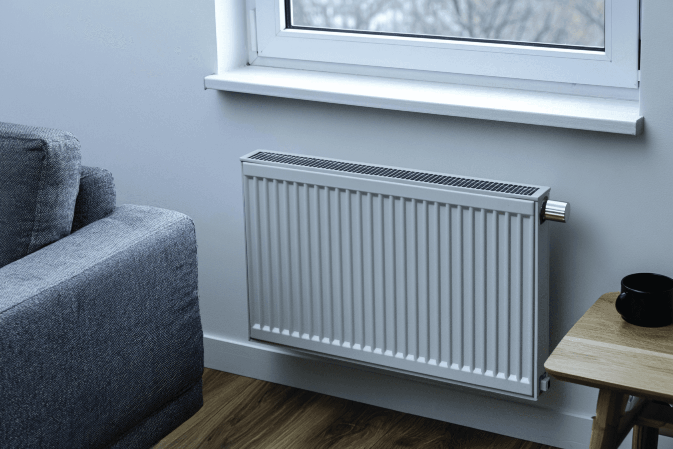 Radiateur mural blanc installé sous une fenêtre dans un salon moderne avec canapé gris et plancher de bois