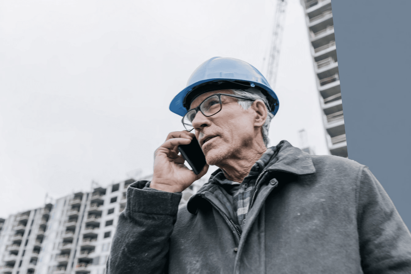 Professionnel de la construction portant un casque de sécurité et parlant au téléphone sur un chantier de bâtiment.