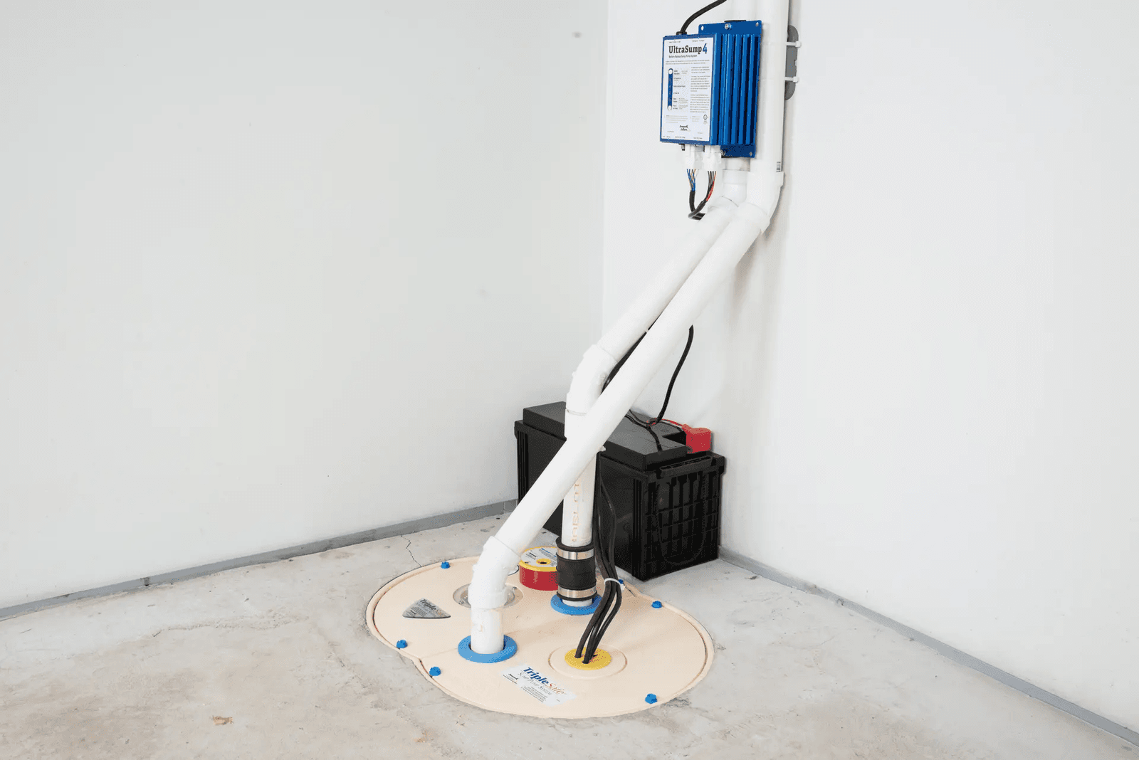  Système de pompe de puisard avec couvercle étanche, tuyauterie en PVC, batterie de secours et contrôleur mural installé dans un sous-sol