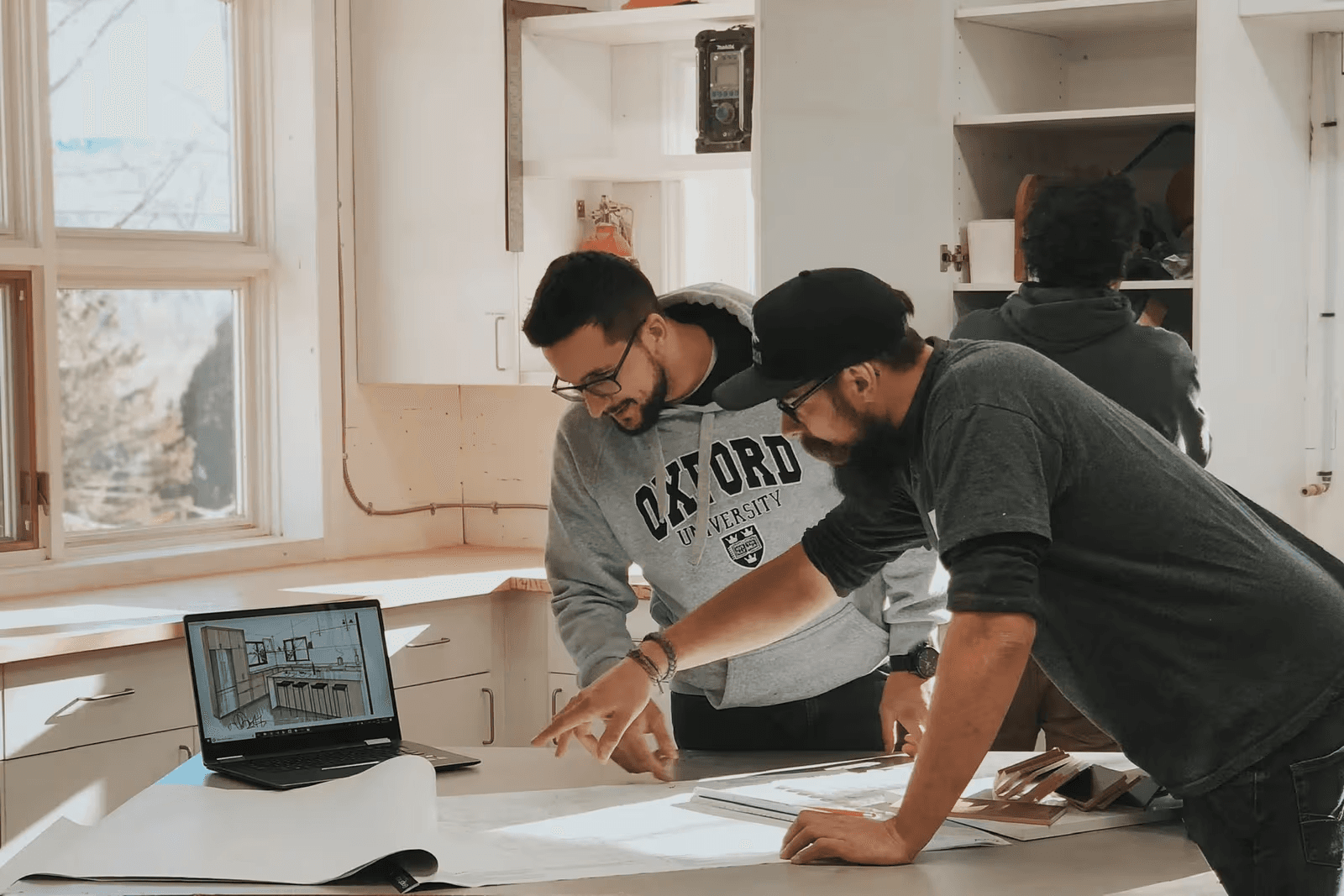 Professionnels de la rénovation examinant des plans et une conception de cuisine sur ordinateur portable dans un espace résidentiel en cours d’aménagement.
