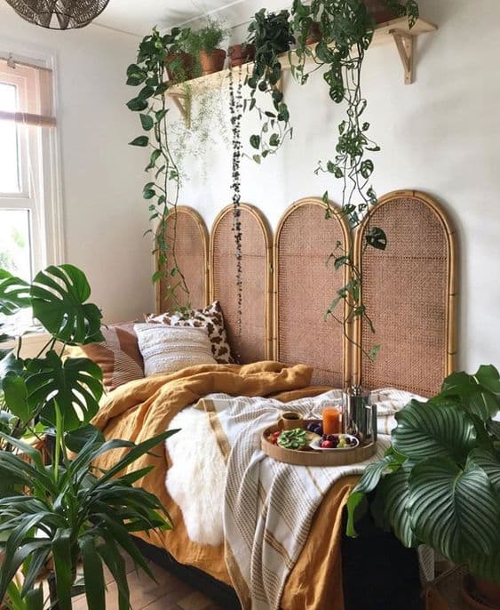 Chambre bohème chaleureuse avec lit confortable, plateau de petit-déjeuner et nombreuses plantes vertes suspendues.