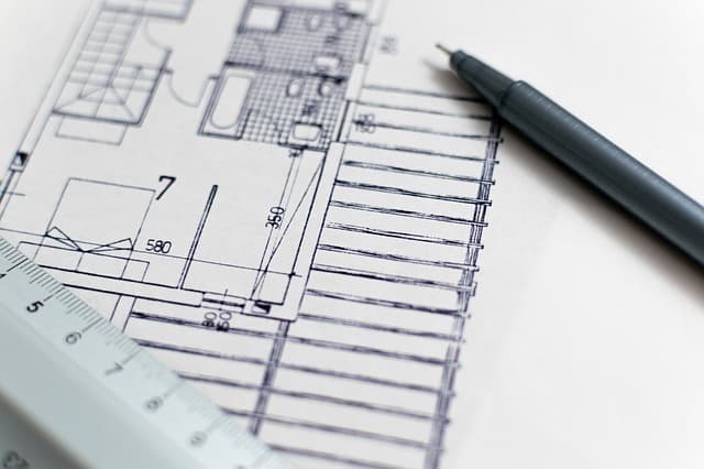 Gros plan d'un plan architectural imprimé montrant les dimensions d'une maison avec une règle blanche et un stylo technique noir posés dessus
