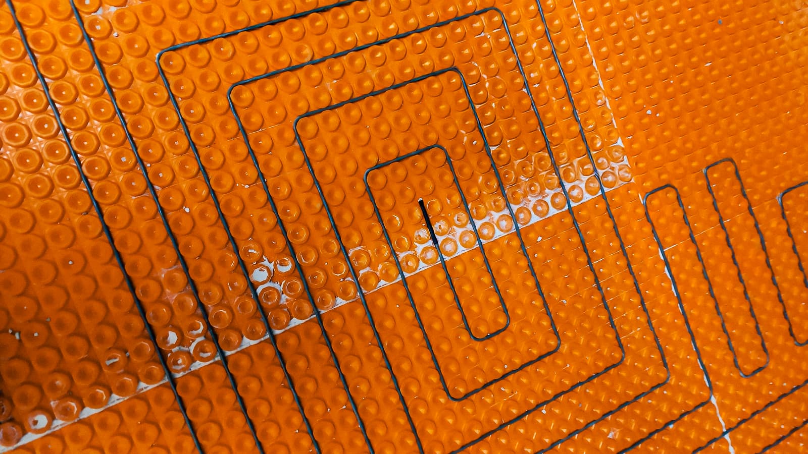 Système de chauffage au sol électrique en cours d'installation, avec câbles intégrés dans une membrane orange.