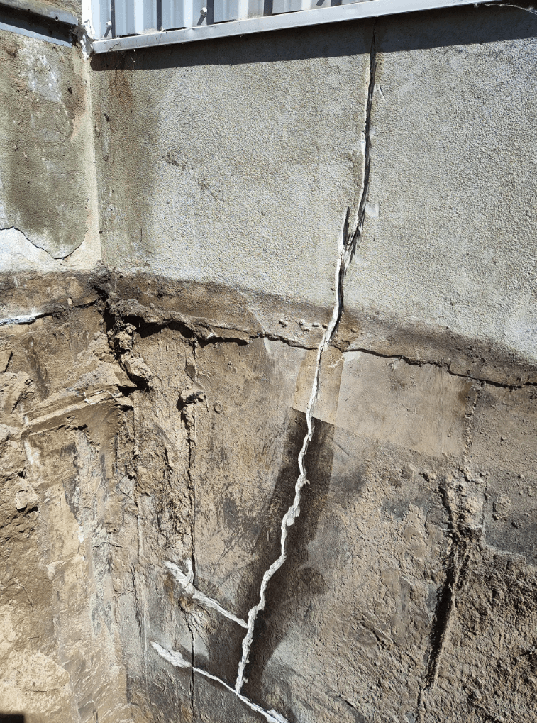 Fissure verticale importante sur une fondation en béton excavée, montrant des signes de dégradation structurelle