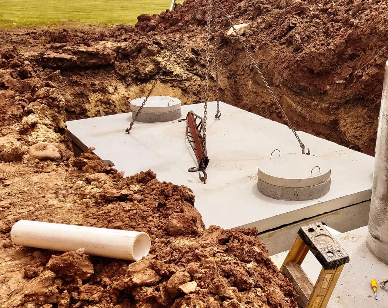 Installation d’une fosse septique en béton avec dalle préfabriquée dans une excavation de terrain résidentiel.