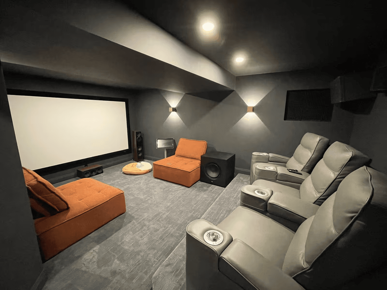 Salle de cinéma maison sombre avec grand écran, fauteuils inclinables, enceintes, éclairage mural et murs acoustiques