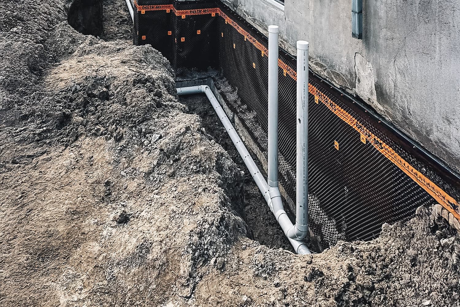 Travaux d'excavation pour l'installation d'un drain français et d'une membrane d'étanchéité sur la fondation d'une maison.