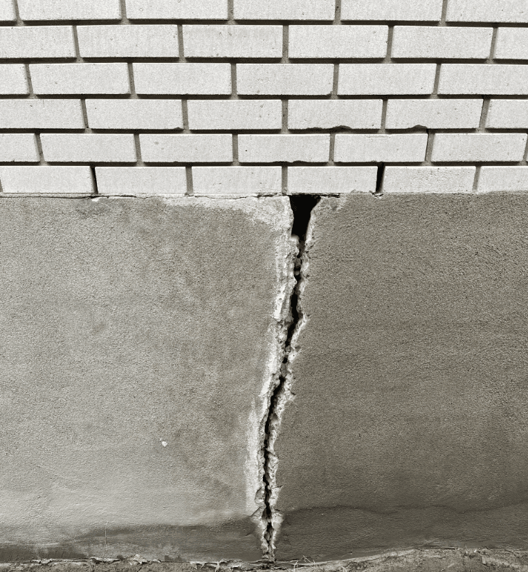 Fissure verticale marquée entre la fondation en béton et le mur de briques d’une maison résidentielle