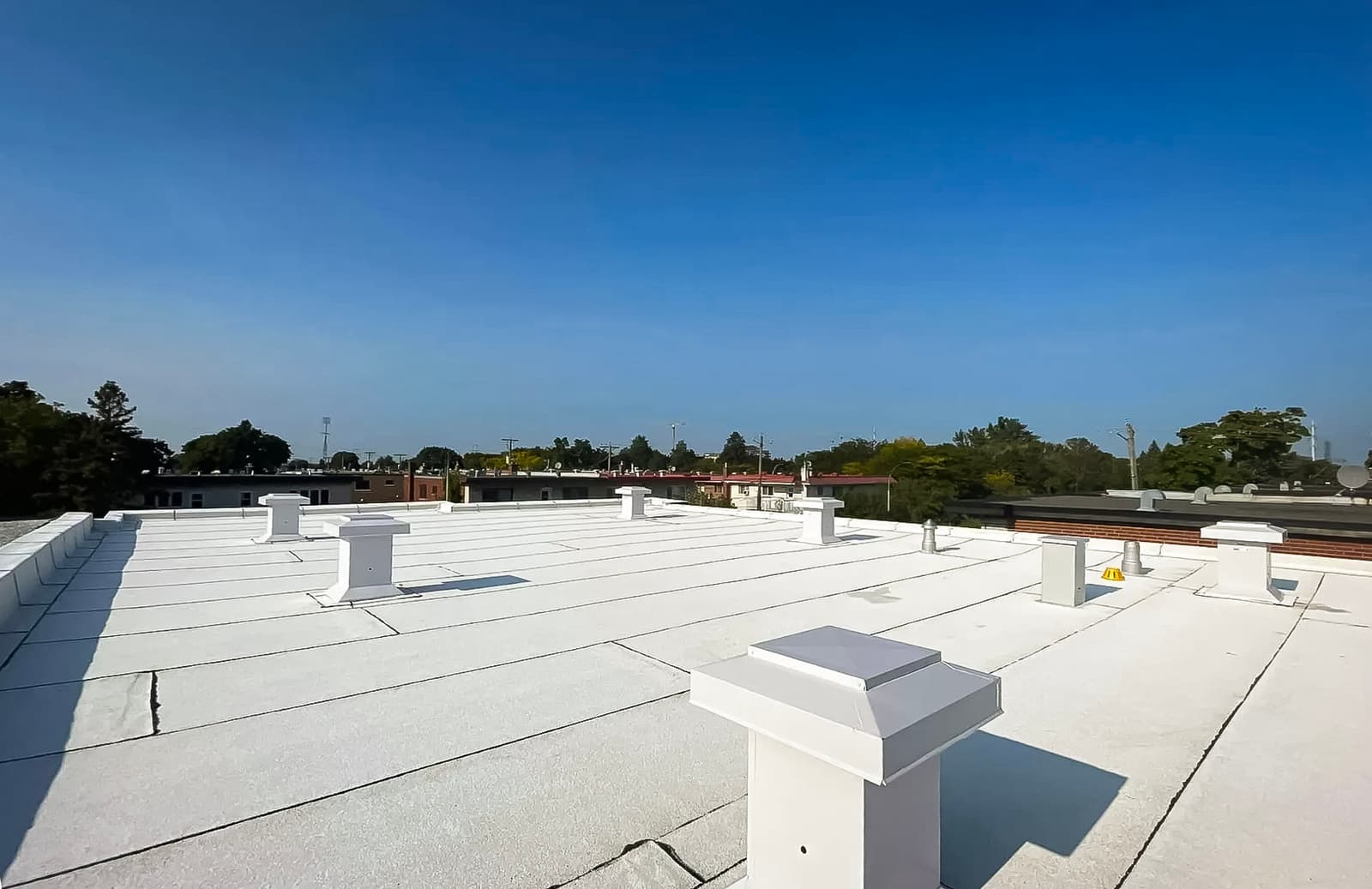 Toiture plate recouverte d'une membrane blanche avec plusieurs évents de ventilation sous un ciel dégagé.<br>