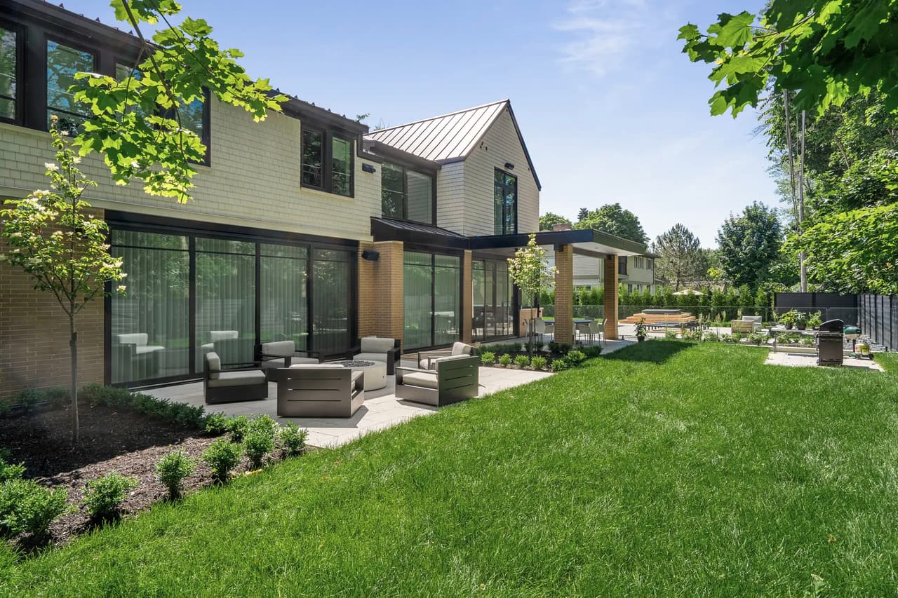 Maison moderne avec grande terrasse, mobilier d'extérieur, gazon bien entretenu et aménagement paysager soigné, entourée d'arbres.