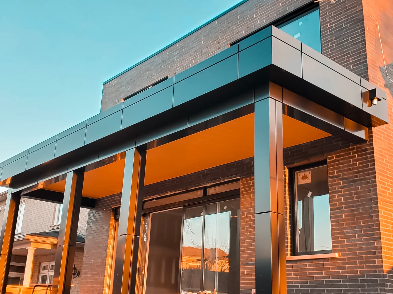 Entrée moderne d’une maison en briques foncées avec structure métallique noire et plafond en bois.