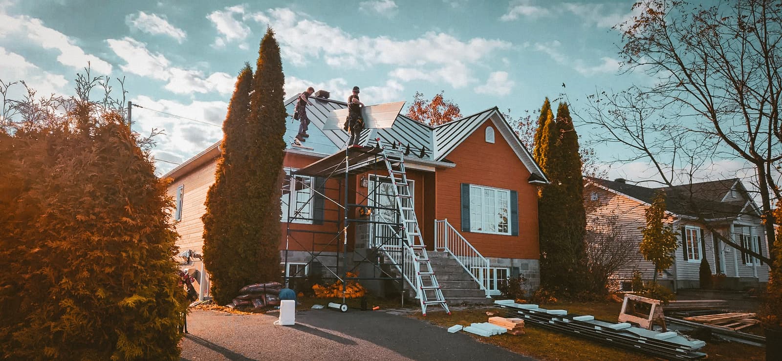 Travaux de rénovation de toiture sur une maison résidentielle avec des ouvriers installant des panneaux de métal, échafaudage et équipement sur place.