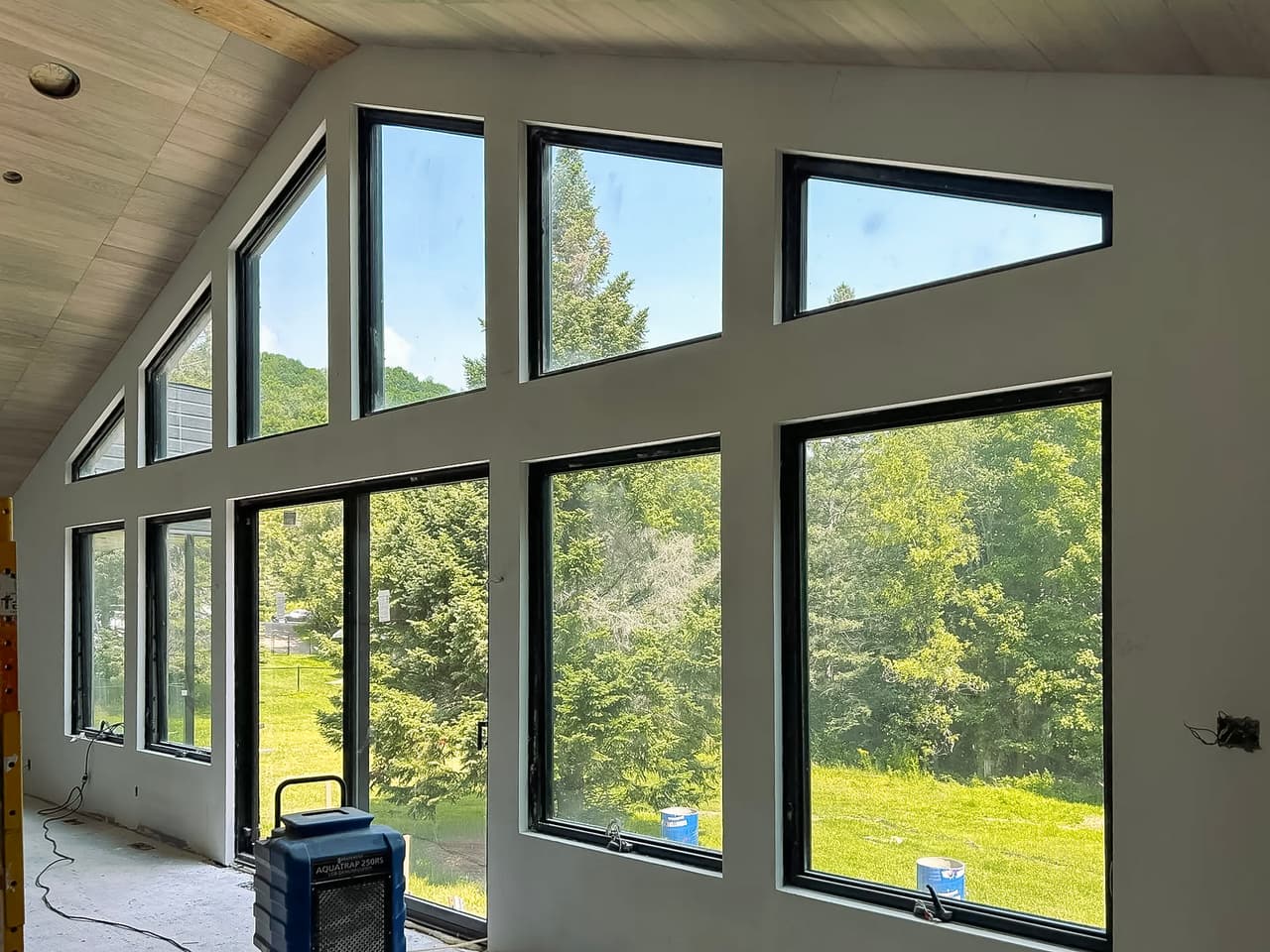 Intérieur d'une maison en construction avec une grande façade vitrée offrant une vue panoramique sur la nature.