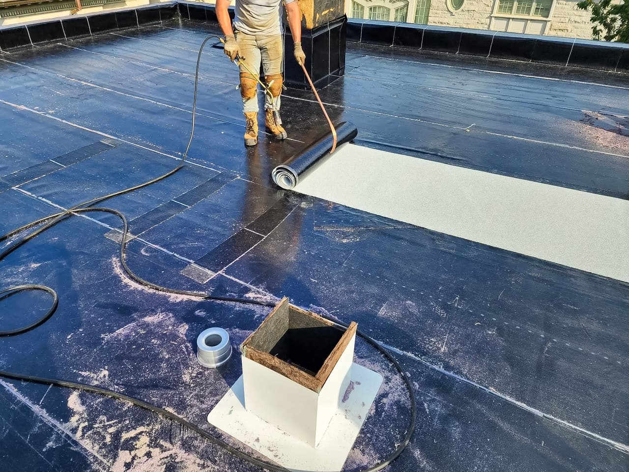 Travaux d'installation d'une toiture en membrane élastomère avec un ouvrier utilisant un chalumeau.