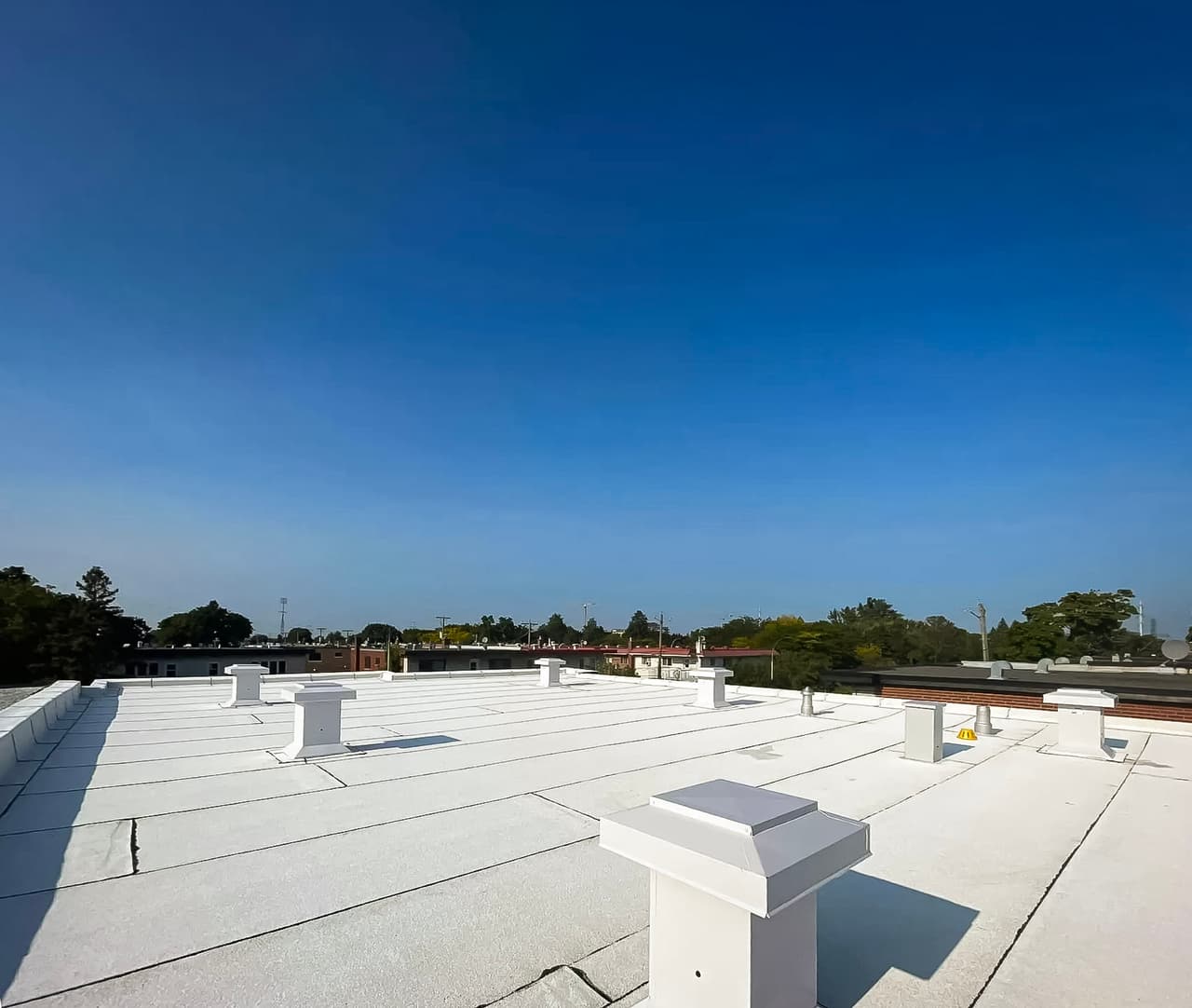 Toiture plate recouverte d'une membrane blanche avec plusieurs évents de ventilation sous un ciel dégagé.