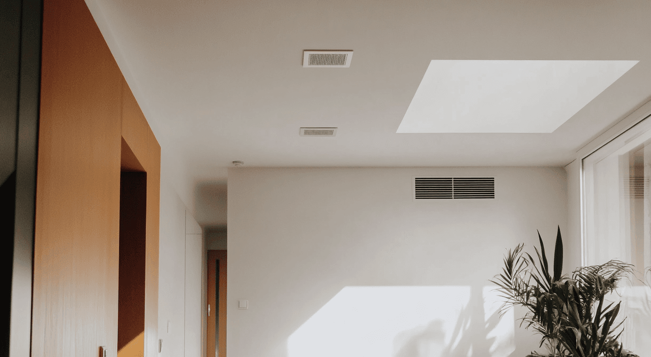 Salon contemporain lumineux avec grilles de ventilation au plafond et mur pour thermopompe gainable