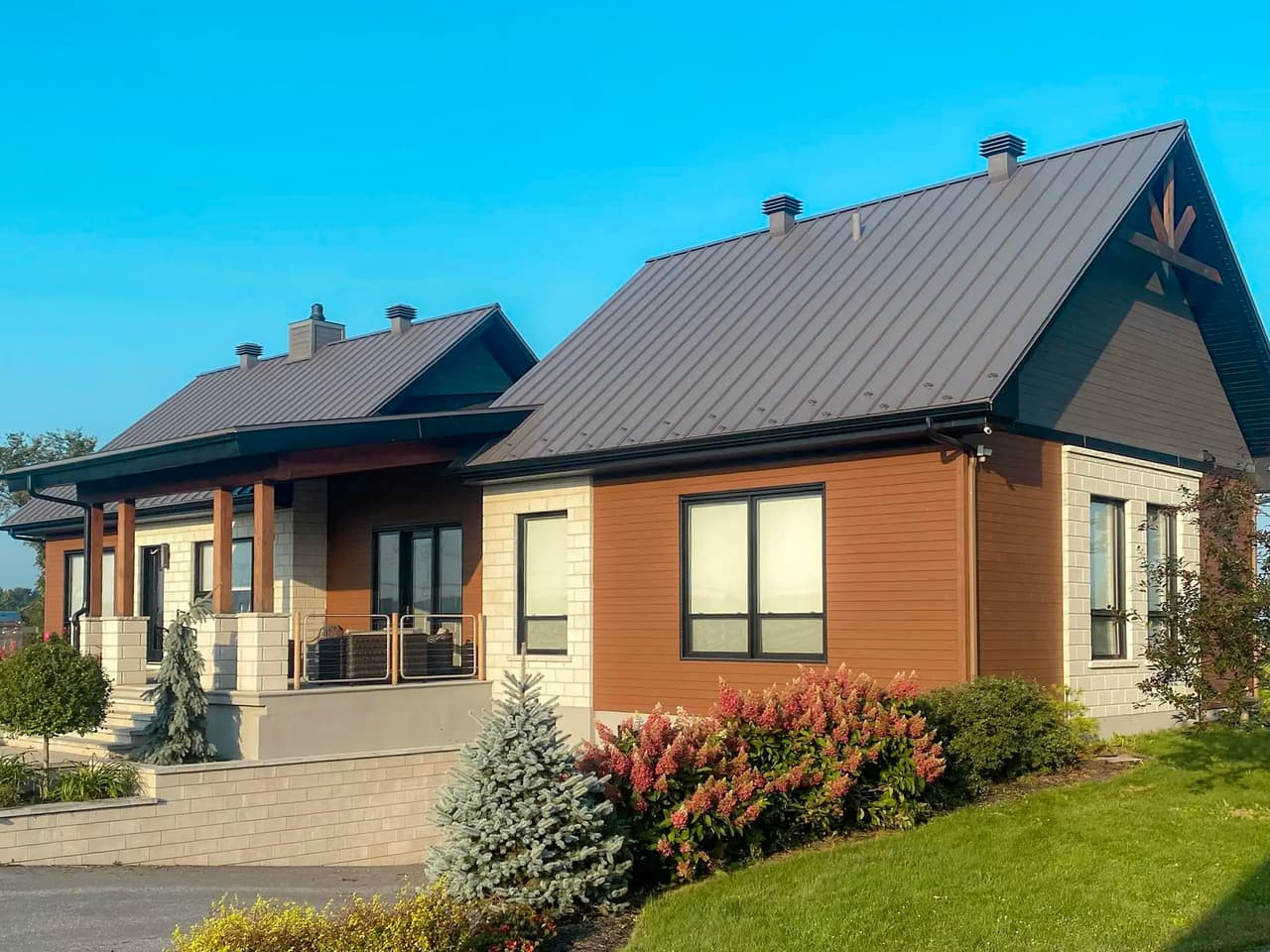 Bungalow moderne en banlieue avec toiture en tôle, revêtement mixte en bois et maçonnerie, aménagement paysager soigné et terrasse couverte.