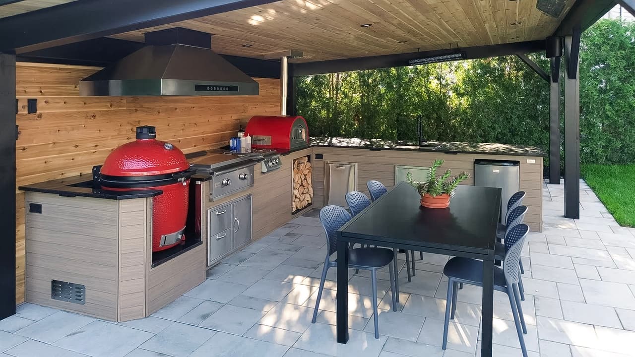 Cuisine extérieure moderne avec barbecue en céramique rouge, four à pizza, comptoirs en bois et coin repas couvert