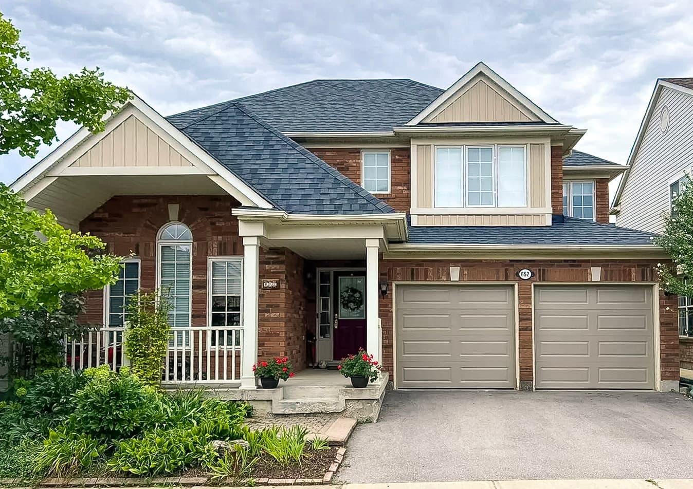 Maison familiale en brique avec garage double, toiture en bardeaux, porche avant et aménagement paysager bien entretenu.