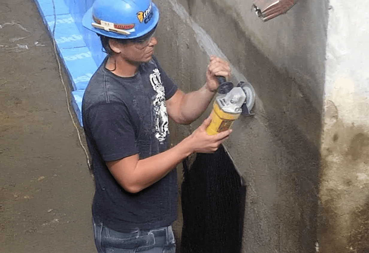 Ouvrier en casque effectuant le meulage d'une fondation en béton pour application d'imperméabilisation
