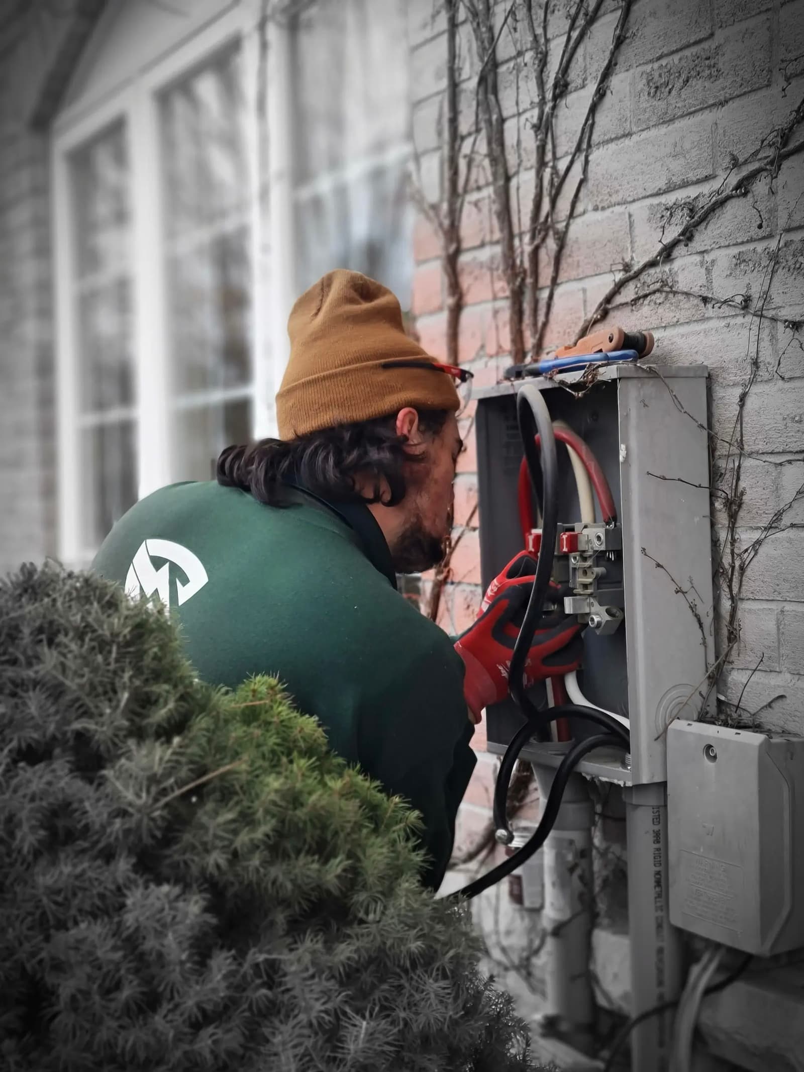 Un électricien effectuant des réparations sur un boîtier électrique extérieur fixé à un mur de briques.