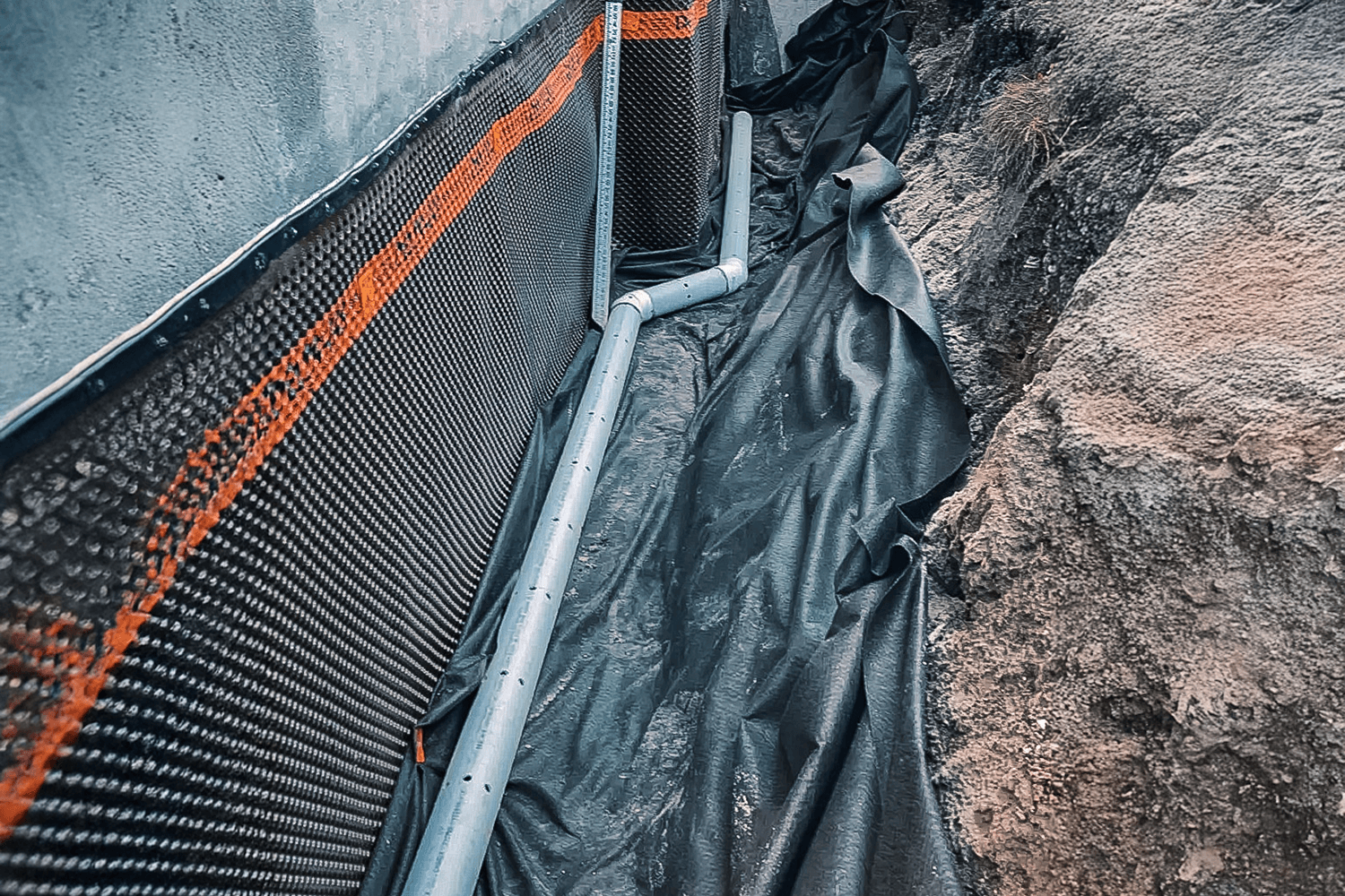 Installation d'un drain français avec membrane d'étanchéité sur la fondation d'une maison.