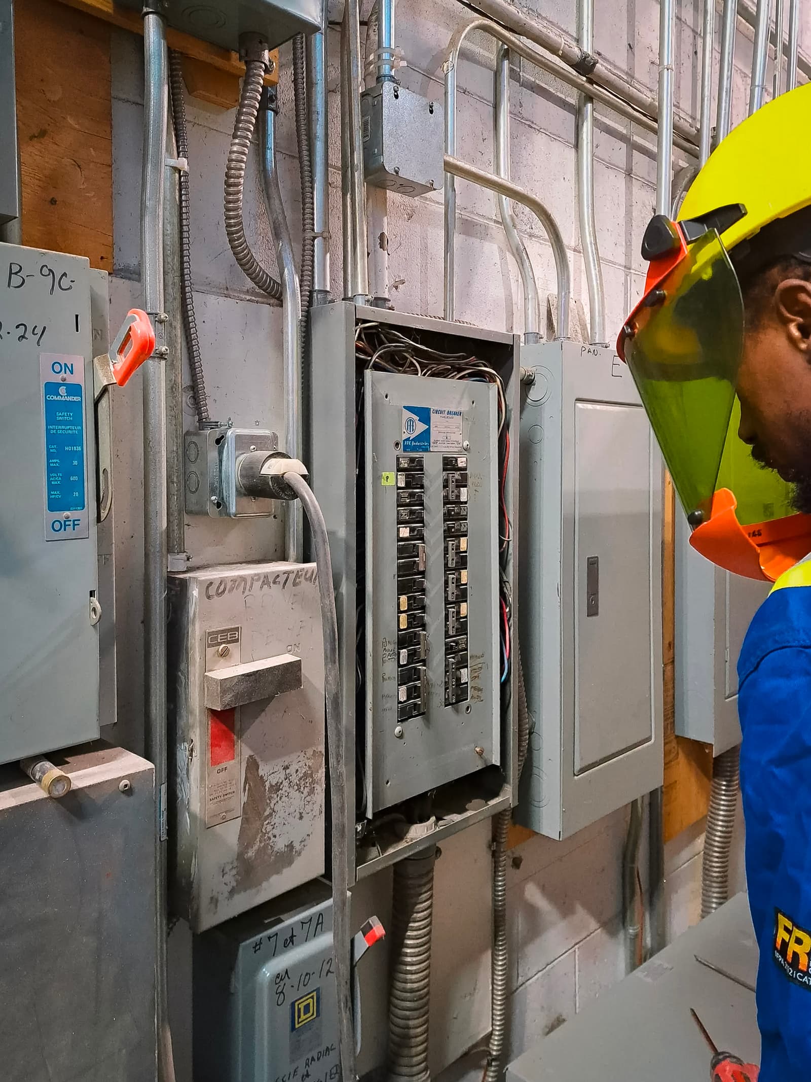 Un technicien en électricité portant de l’équipement de protection inspecte un panneau électrique industriel.