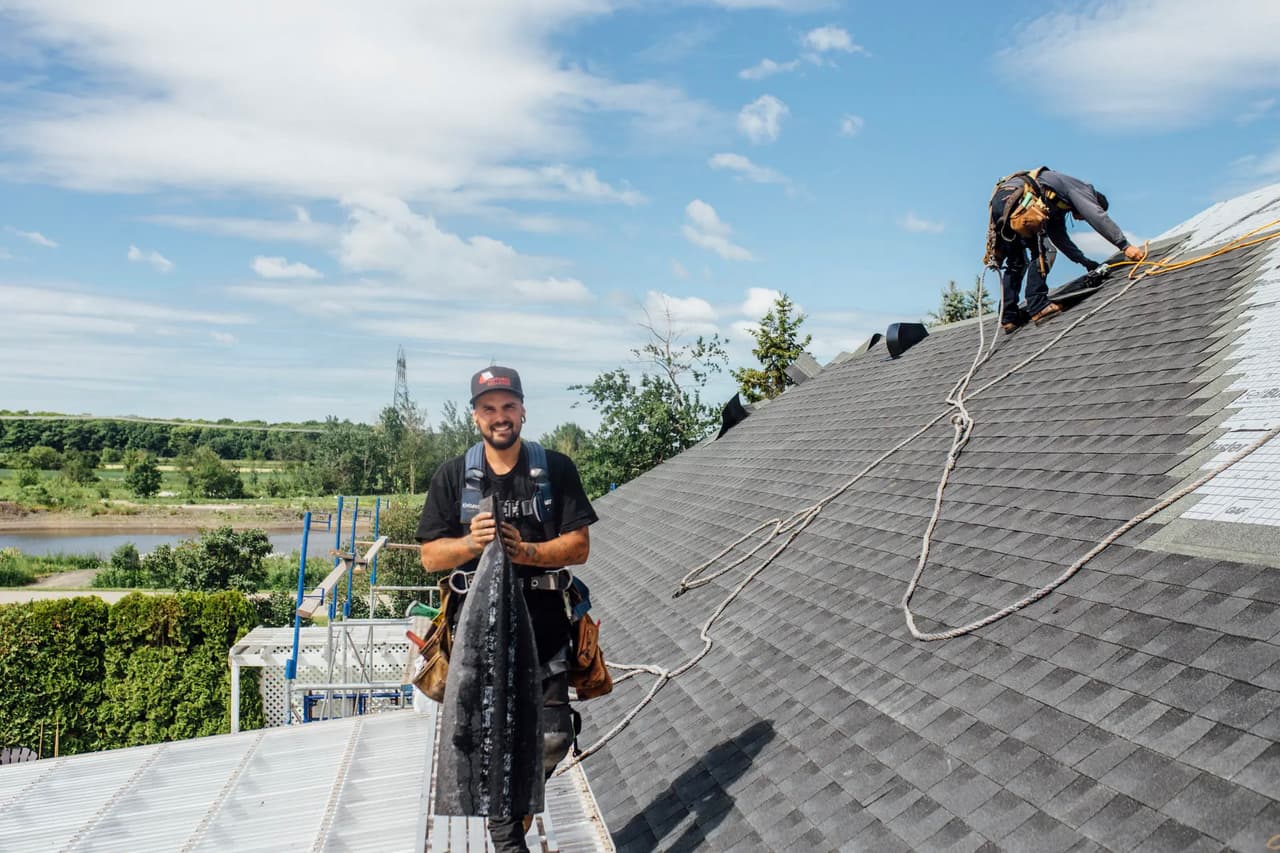 Travailleurs installant un toit en bardeaux gris sur une maison sous un ciel dégagé