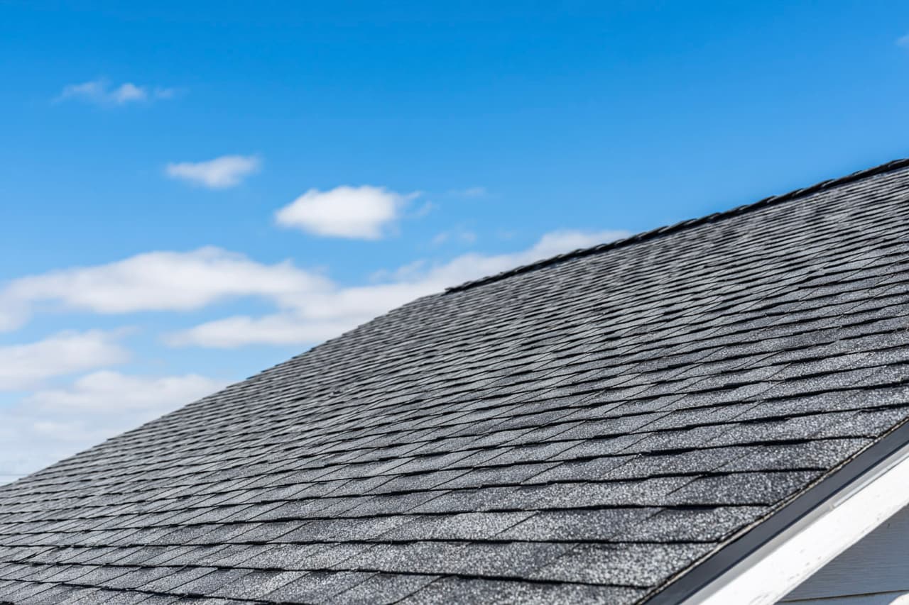 Toiture résidentielle en bardeaux d’asphalte gris sous un ciel bleu clair