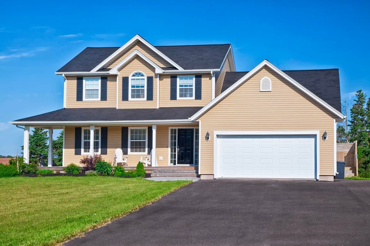 Maison familiale moderne avec garage double, allée en asphalte neuve et aménagement paysager soigné sous un ciel bleu.