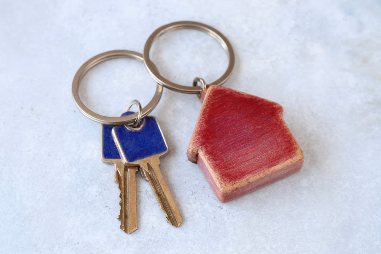 Porte-clés en forme de maison rouge avec trousseau de clés métalliques sur surface claire, symbole de propriété, logement et sécurité résidentielle