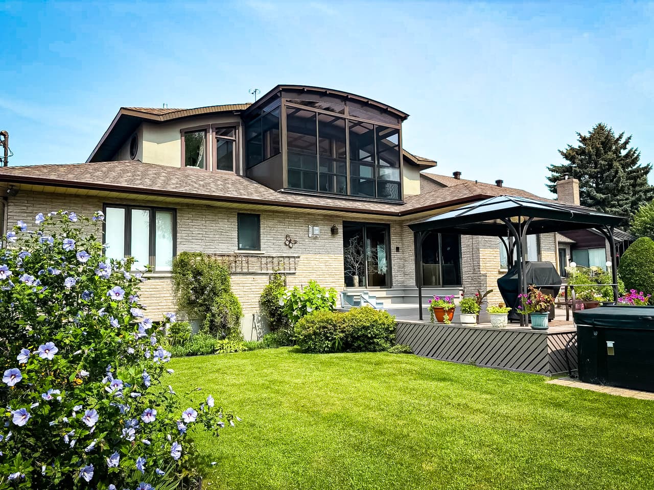 Maison familiale avec véranda fermée, terrasse, gazebo moderne et jardin paysager.