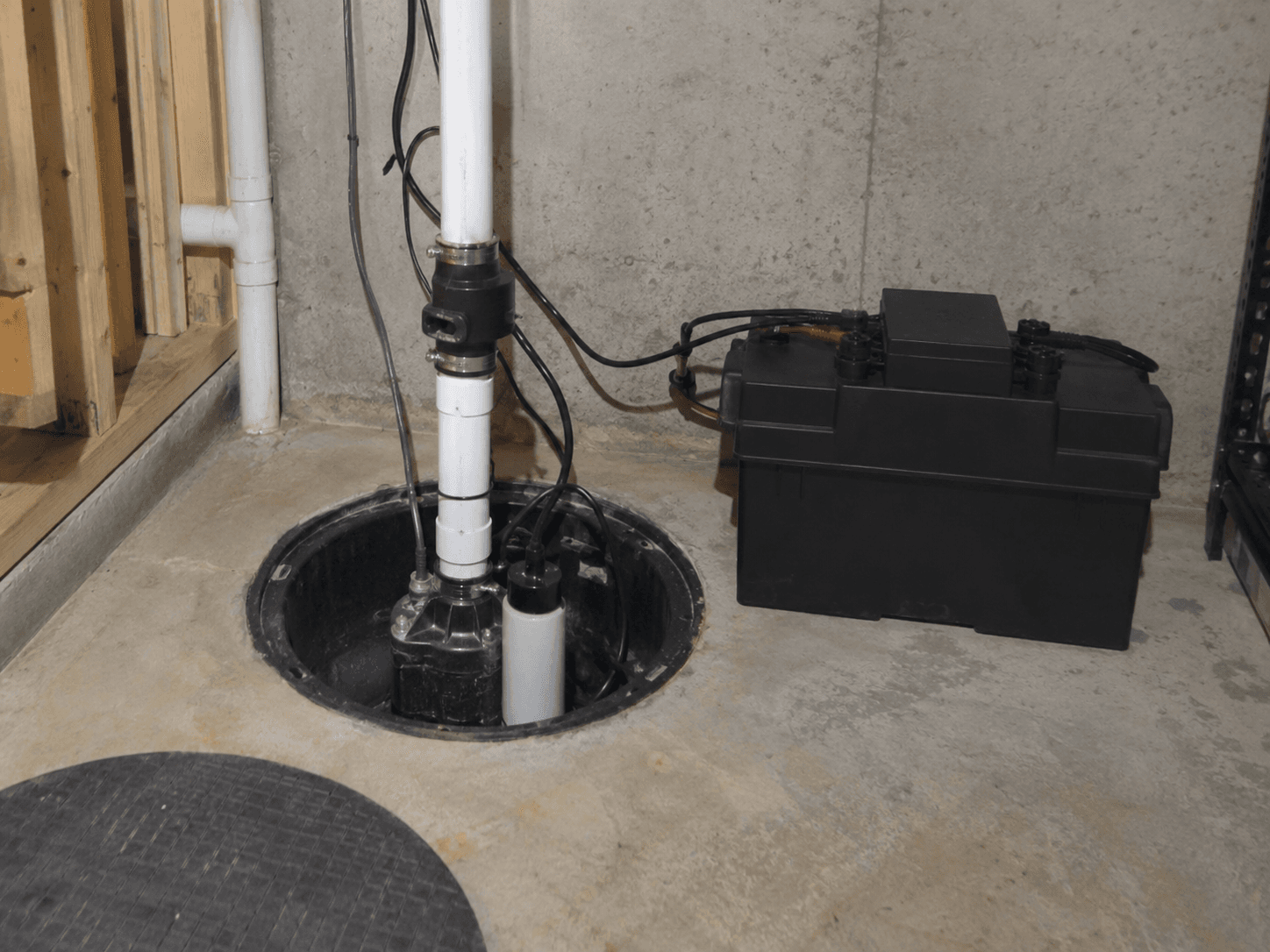 Système de pompe de puisard installé dans un bassin de sous-sol avec tuyauterie en PVC et batterie de secours pour prévenir les infiltrations d’eau