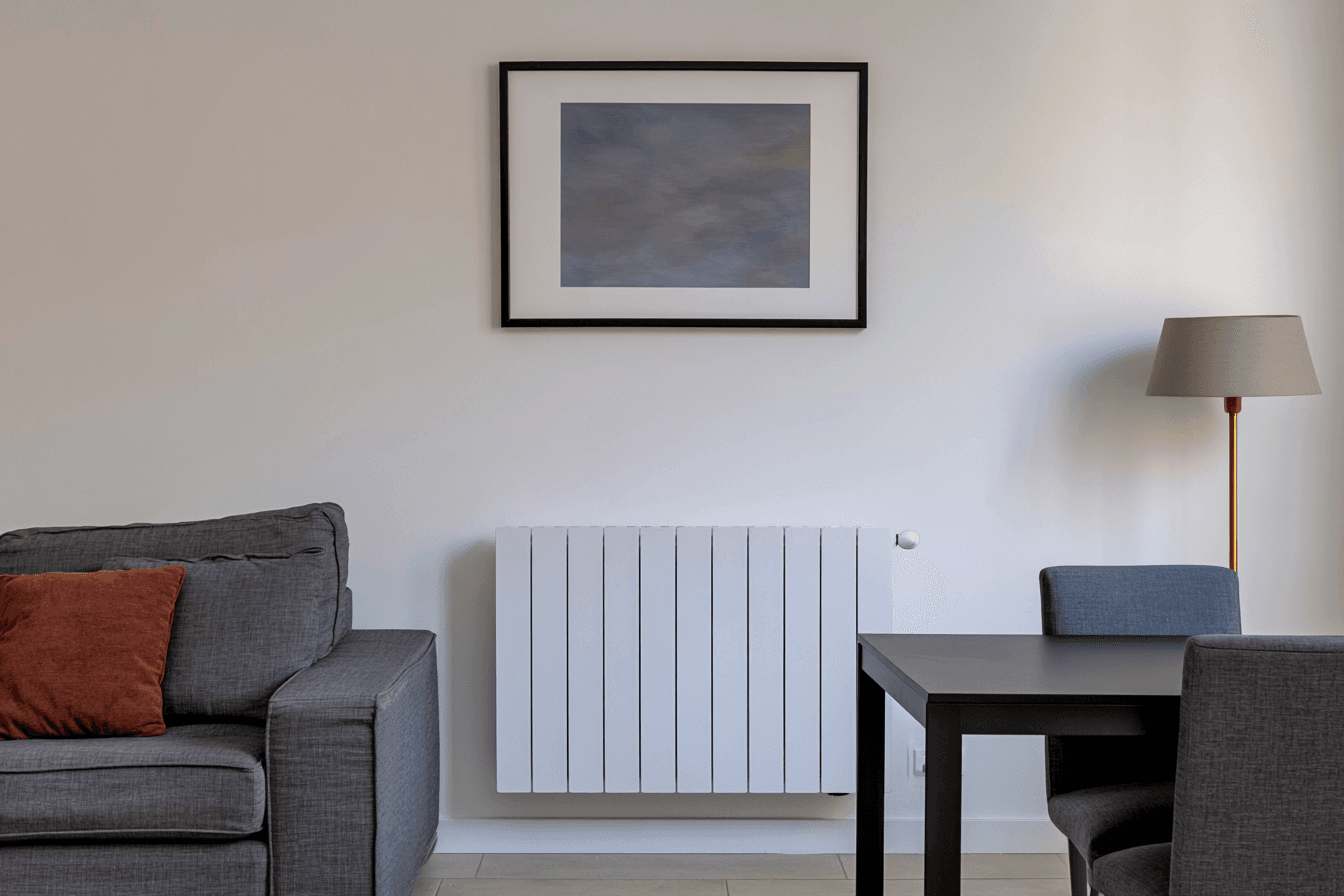 Radiateur mural blanc installé dans un salon moderne avec canapé gris, table noire, lampadaire et décoration intérieure minimaliste